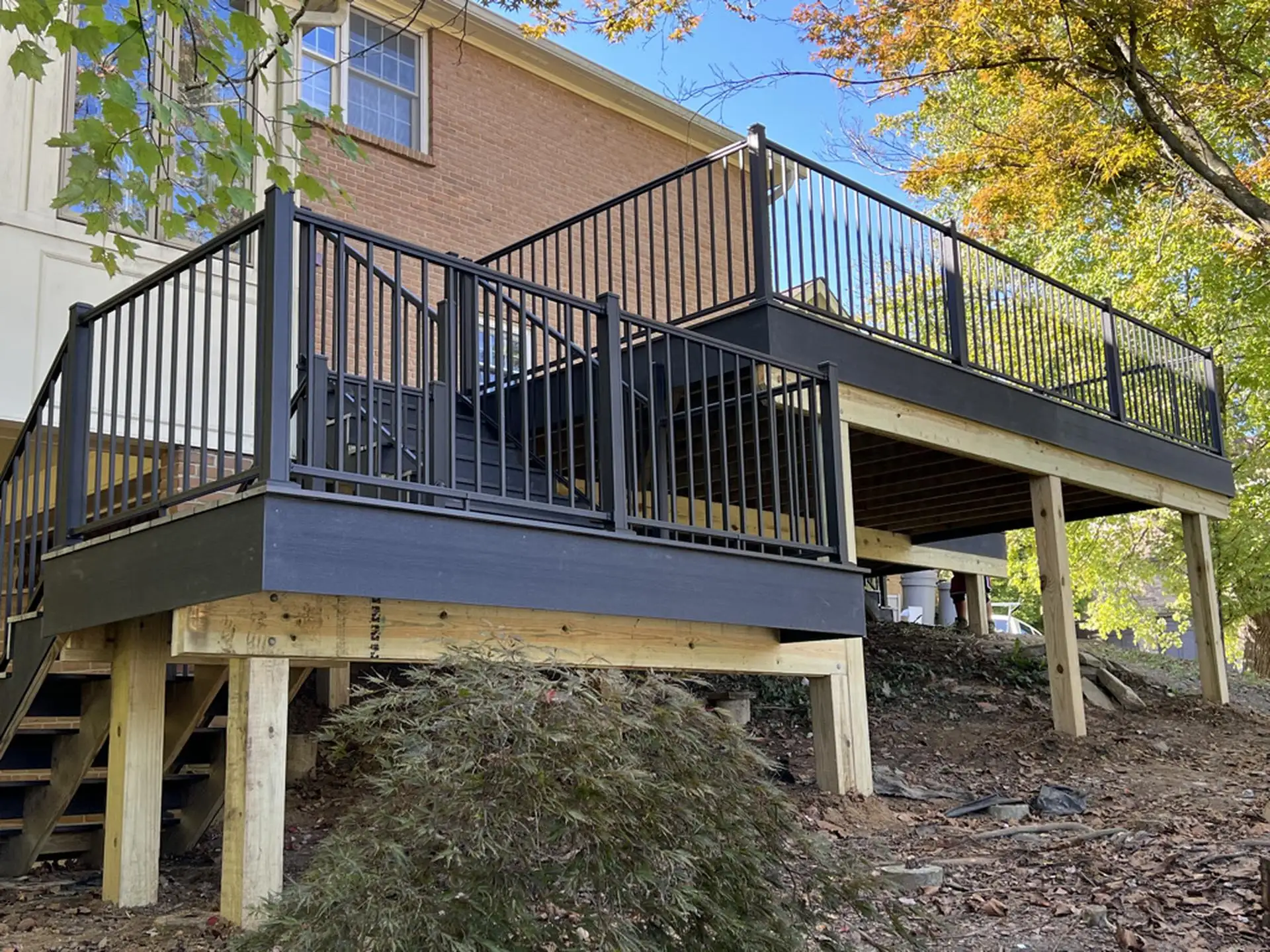 Black metal deck railings on a two-level deck, with stairs leading down to the ground and surrounded by a scenic landscape of trees.