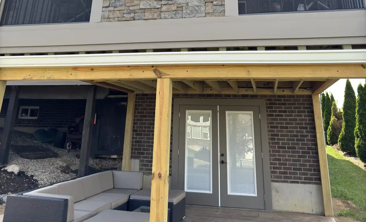 A two-story outdoor living area featuring an upper screened-in porch with a central stone wall and a lower covered patio with seating.
