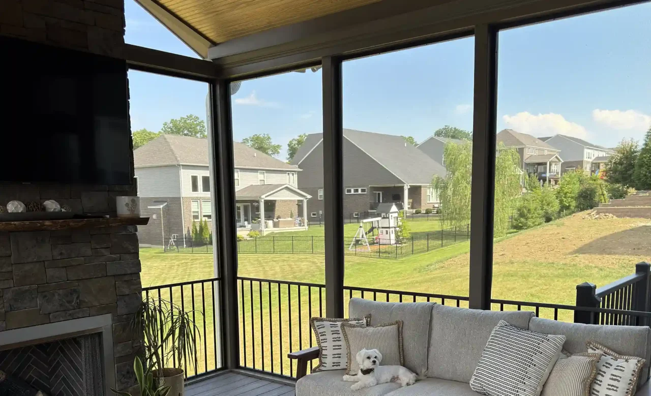 Screened-in porch featuring a stone fireplace with a TV mounted above, a modern rug, and comfortable seating, with a large window.