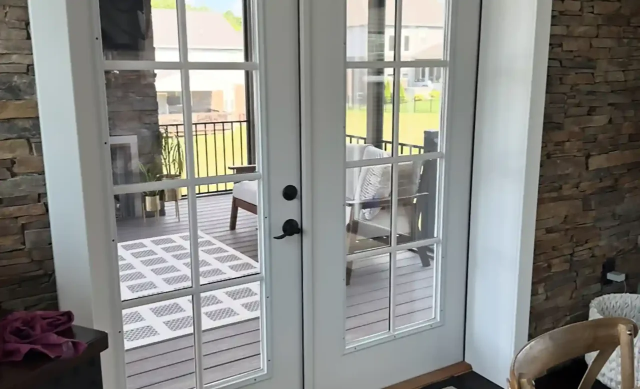 Double French doors with glass panels leading to a screened-in porch with a stone wall and modern rug.