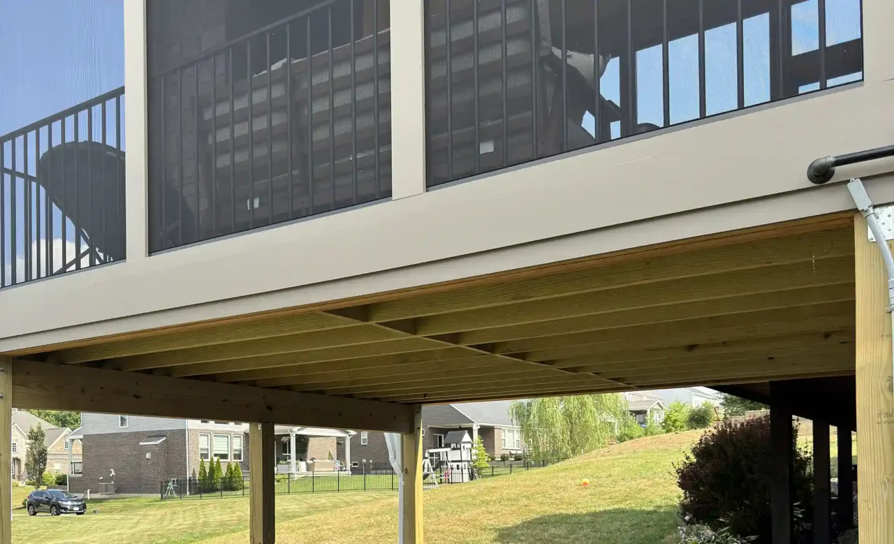 View of a covered patio beneath a screened-in porch, featuring sectional seating on a stamped concrete floor and wooden support beams above.