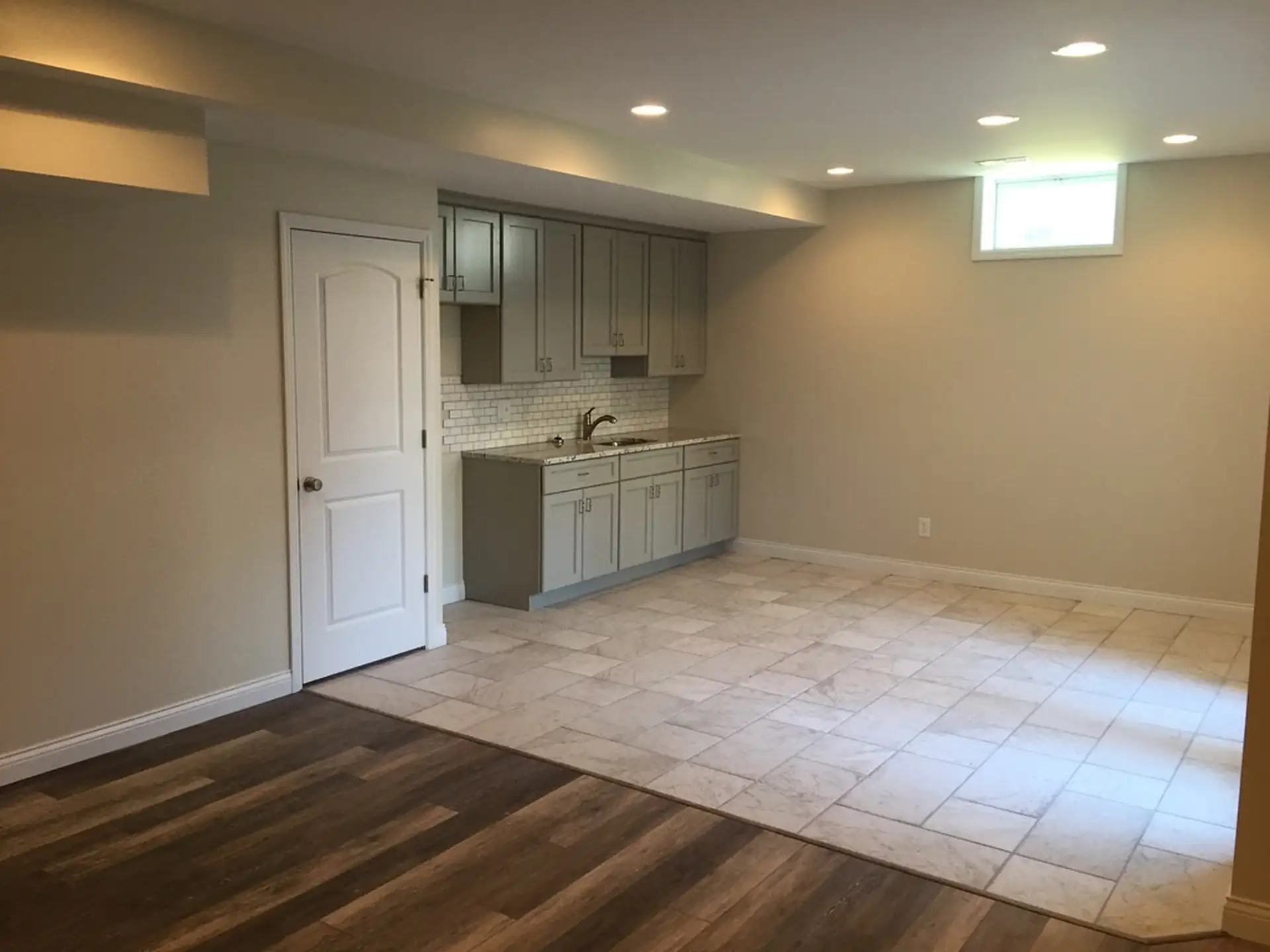 Finished basement kitchenette with gray shaker cabinets, white subway tile backsplash, stainless sink and faucet, recessed lighting and mixed tile and wood-look flooring